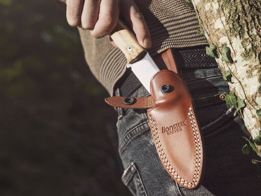 LionSteel fixed blade knife with olive wood handle being drawn from a brown leather belt sheath outdoors