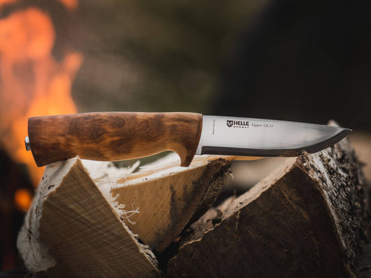 Fixed blade outdoor knife with a wooden handle resting on split firewood in front of a campfire