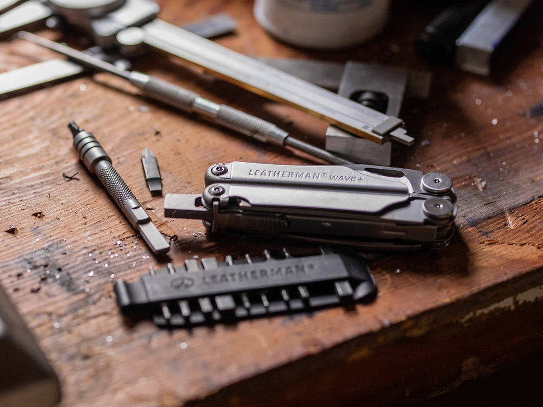 Leatherman Wave Plus multi-tool and bit kit lying on a worn wooden workbench next to metalworking tools