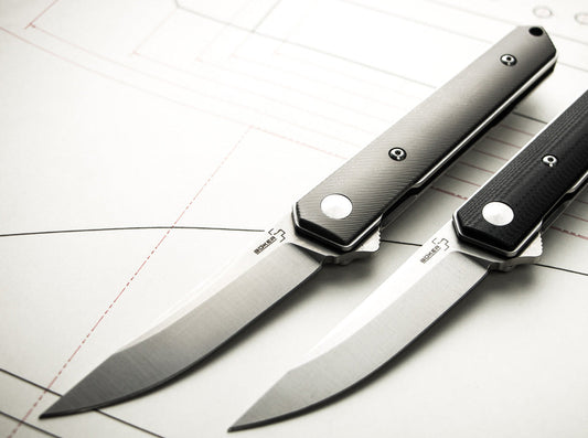 Two Boker Plus folders with titanium and black G10 handles on a technical drawing