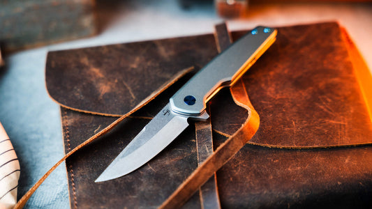 Boker Plus titanium folder resting on brown leather in warm light